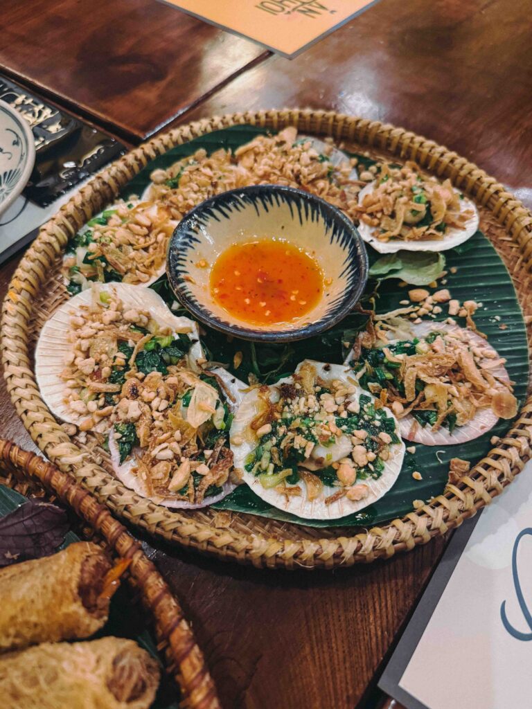 Grilled scallops in the shell topped with scallion oil and crushed peanuts arranged on a banana leaf at Ăn Thôi Da Nang