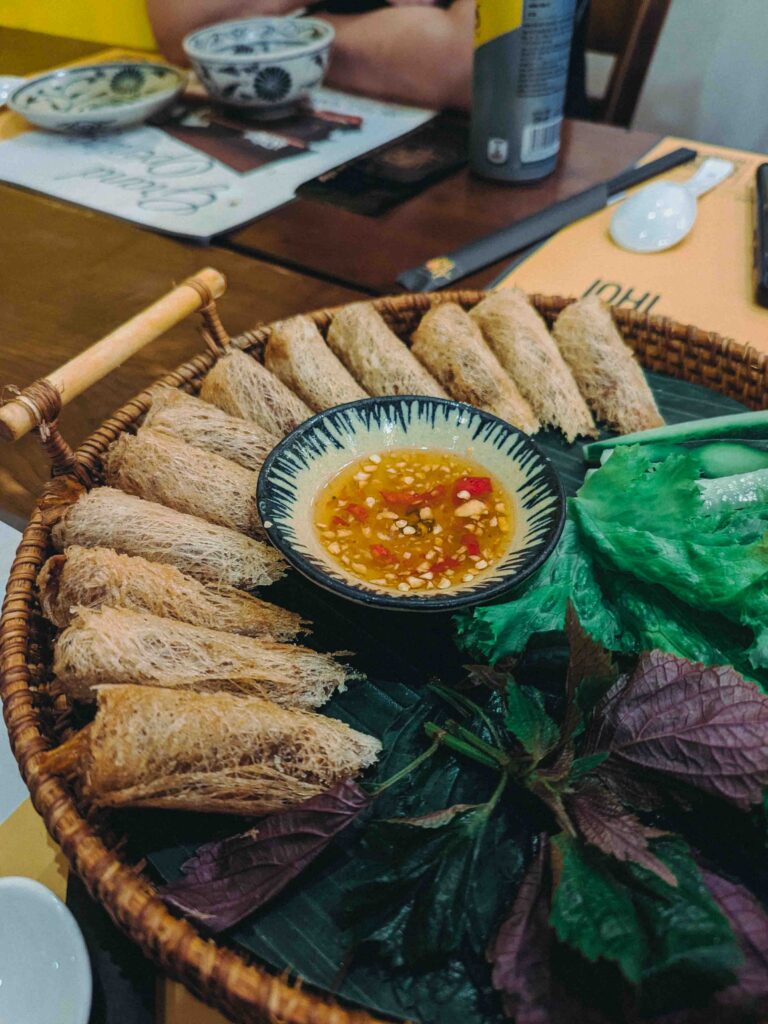 Vietnamese fried spring rolls with a crispy vermicelli coating arranged on a banana leaf with herbs and dipping sauce at Ăn Thôi Da Nang