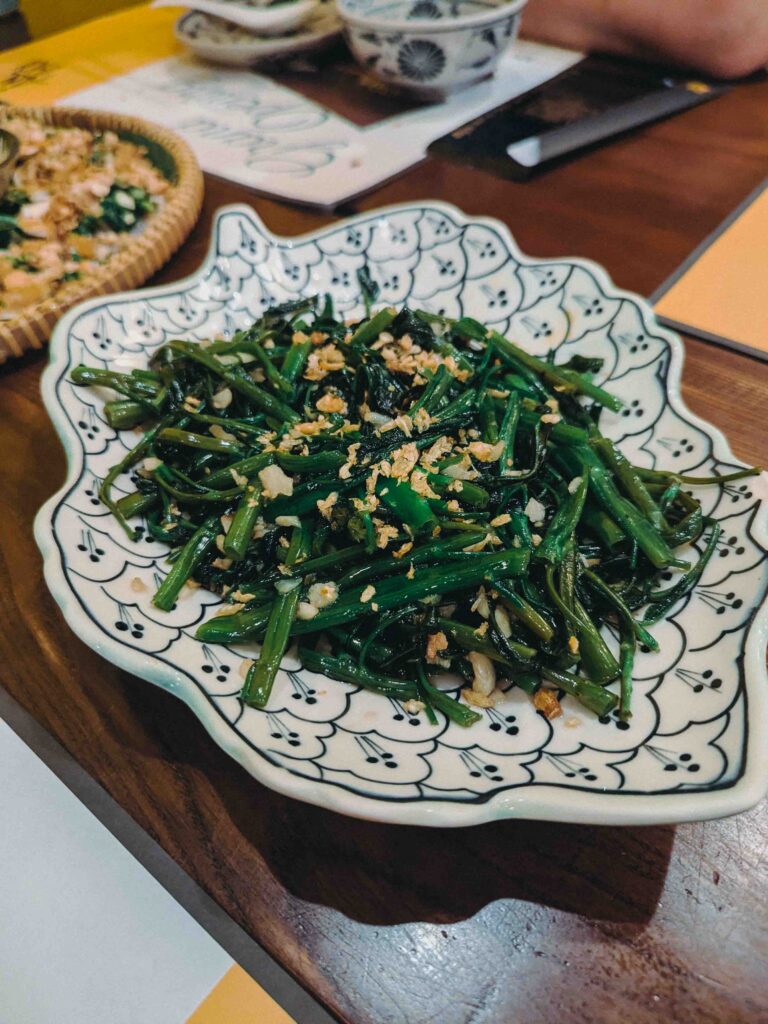 Stir-fried morning glory with crispy garlic served in a patterned ceramic dish at Ăn Thôi Da Nang