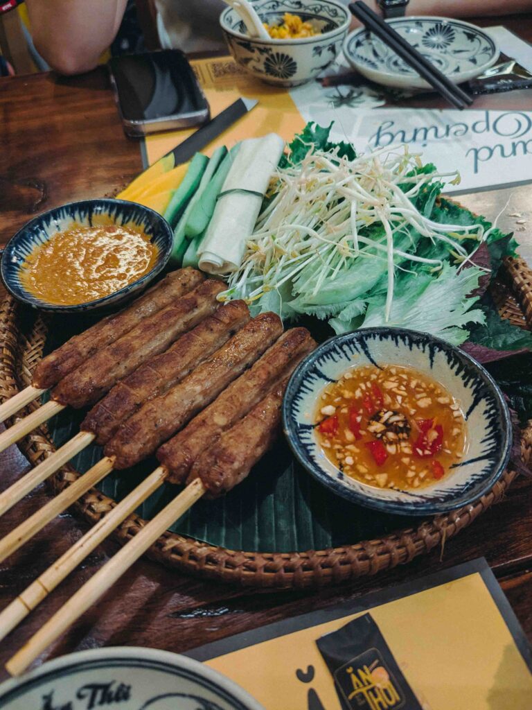 Lemongrass pork skewers served with fresh herbs, rice paper, and two dipping sauces at Ăn Thôi Da Nang
