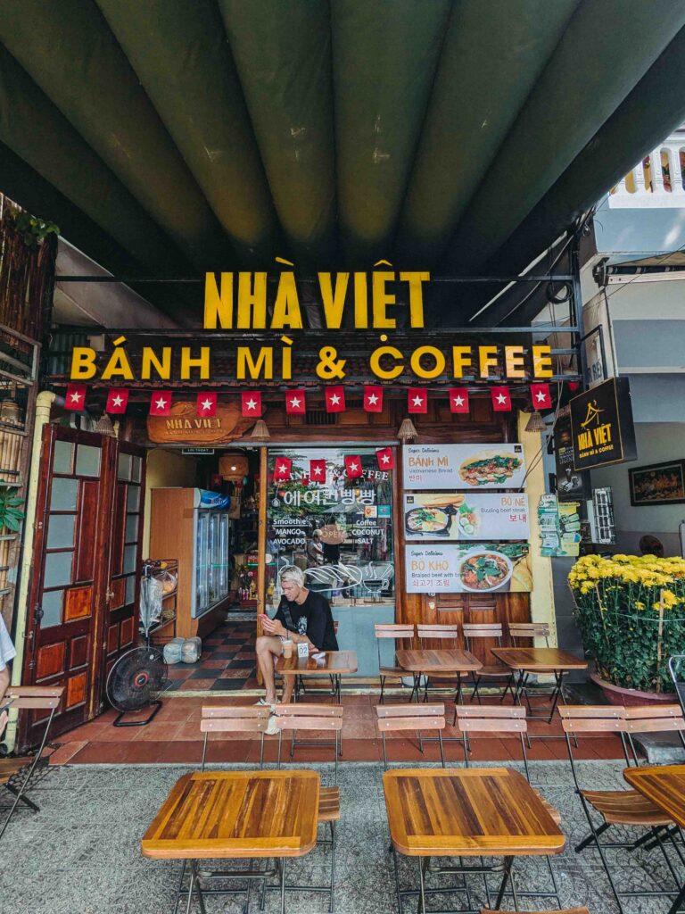 Nhà Việt Bánh Mì and Coffee shop exterior in Da Nang with yellow signage wooden tables and Vietnamese flag bunting