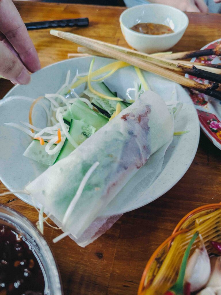 Hand wrapping grilled pork in rice paper with herbs at Quán Phú Hồng Da Nang