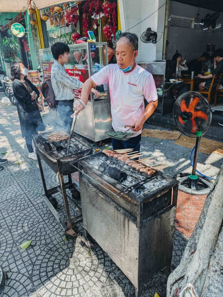 Quán Phú Hồng owner grilling pork skewers on charcoal outside the restaurant in Da Nang