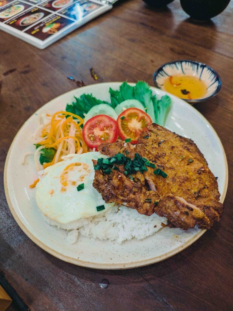 Broken rice topped with grilled pork chop and fried egg served with fresh salad and dipping sauce at Cơm Linh Hội An