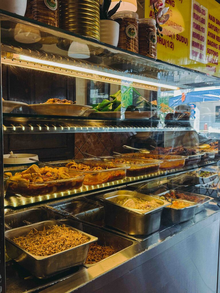 Nasi lemak sides display counter at Village Park Restaurant showing ikan bilis, sambal, and various lauk